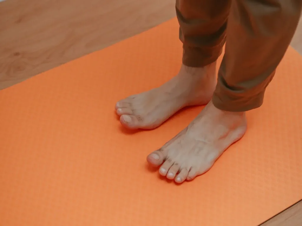 Bàn chân trần đứng trên tấm thảm yoga màu cam trải trên sàn gỗ