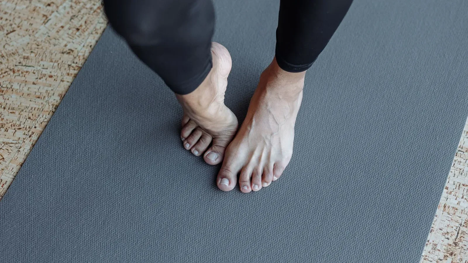 Bàn chân trần đứng trên tấm thảm yoga màu xám, nhìn từ trên xuống