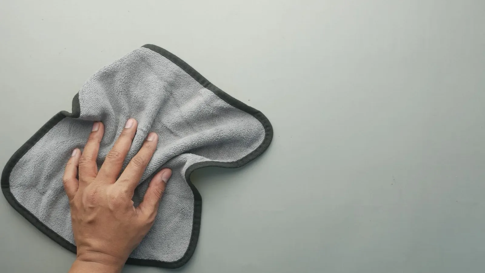Bàn tay dùng khăn microfiber màu xám lau một bề mặt phẳng